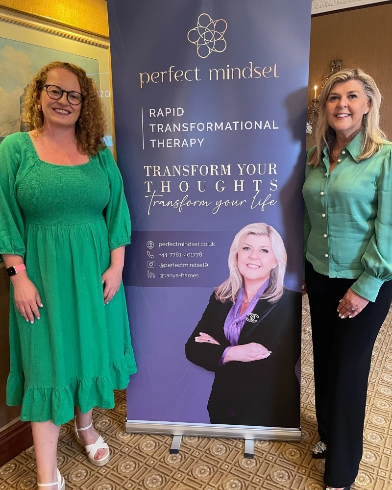 Two women in green standing in front of a Perfect Mindset banner