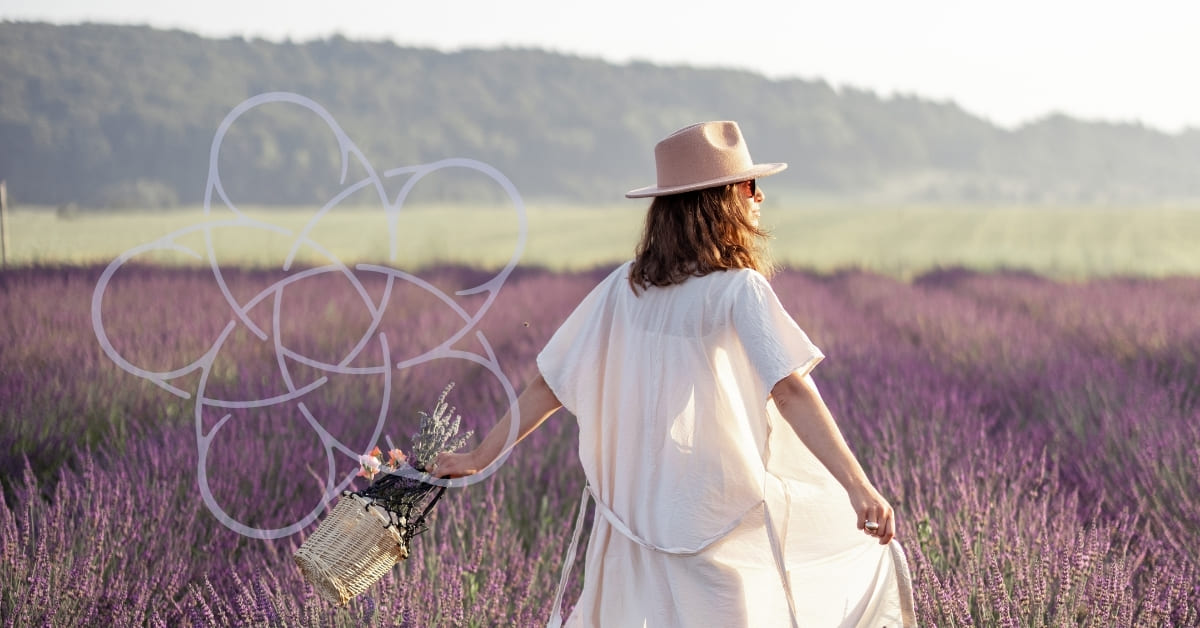 A woman in a light dress and hat walks through a lavender field, holding a basket of flowers. She faces away, with trees and a misty sky in the background. A geometric white design overlays part of the image.