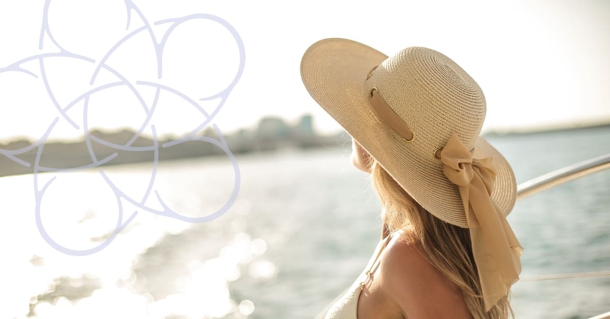 A woman with long blonde hair wearing a hat looks over a body of glistening water at sunset. She faces away. A geometric lilac design overlays part of the image.